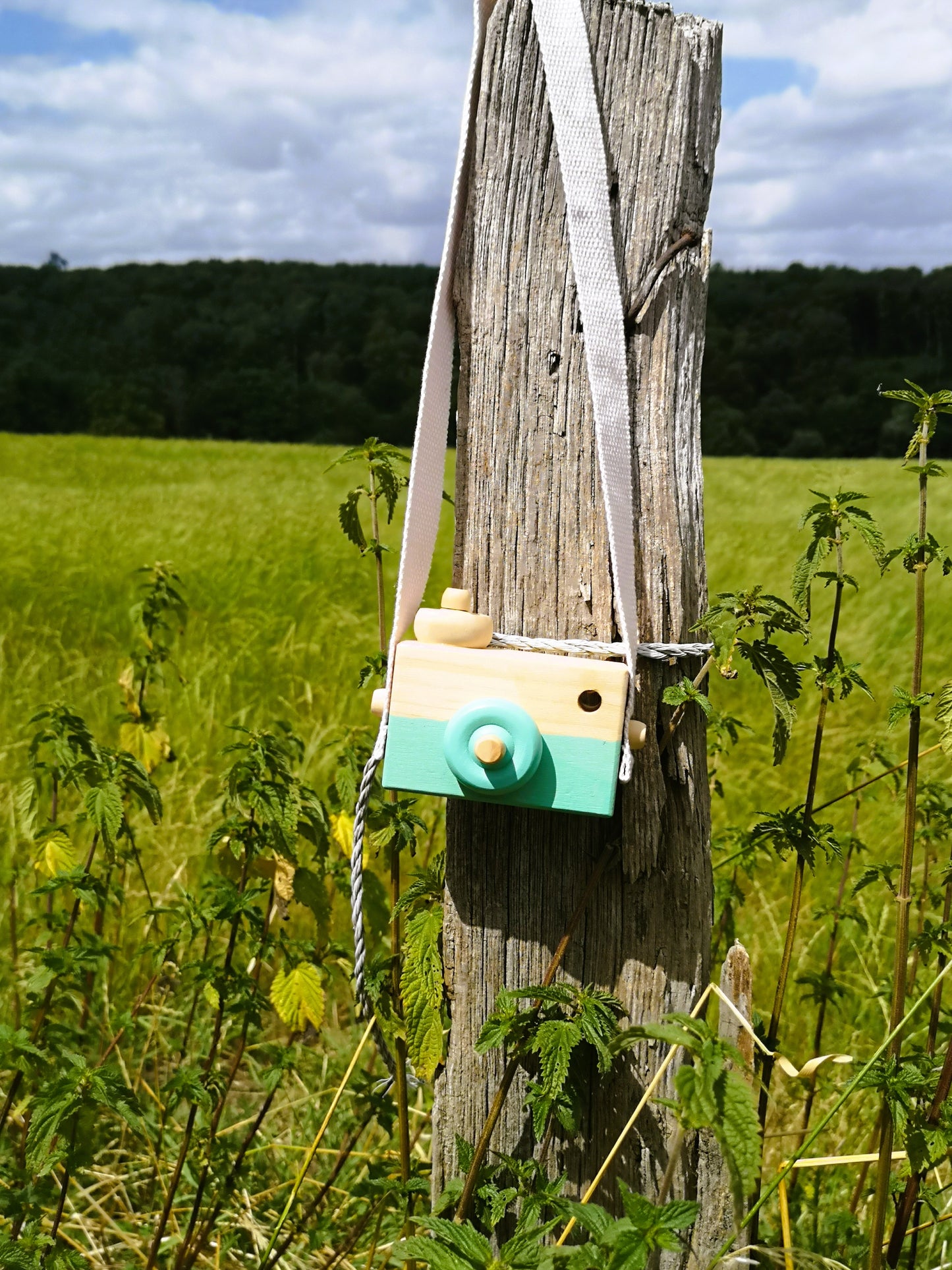 Holzkamera um den Hals eines Kindes, draußen mit Strohhut – stilvolles, sicheres Spielzeug