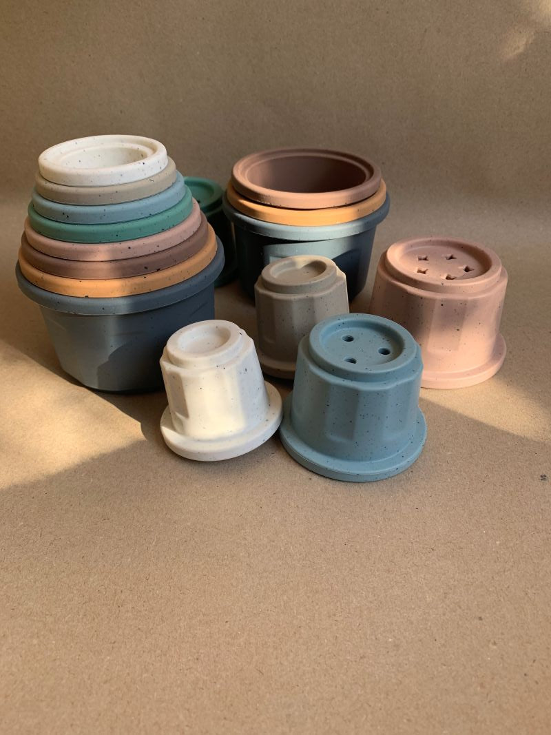 Silikonbecher in Pastell- und Naturtönen nebeneinander arrangiert – Lernspielzeug für Babys ab 6 Monaten