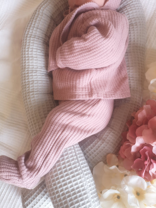 Baby liegt in grauem Waffelpiqué-Nestchen mit rosafarbener Kleidung – weich und gemütlich