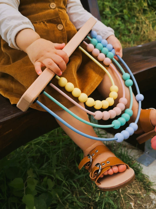 Kind hält bunten Holz-Abakus auf dem Schoß, perfekt als Lernspielzeug für Kleinkinder ab 1 Jahr