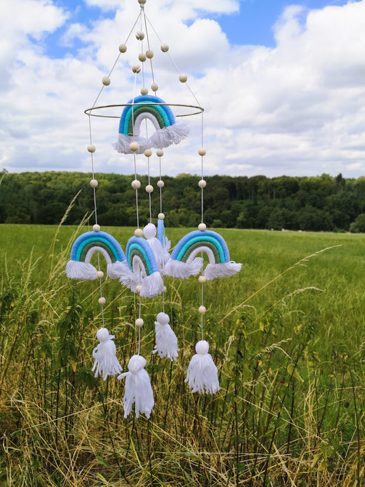 Blaues Makramee-Mobile mit Regenbögen, weißen Quasten und Holzperlen vor blauem Himmel
